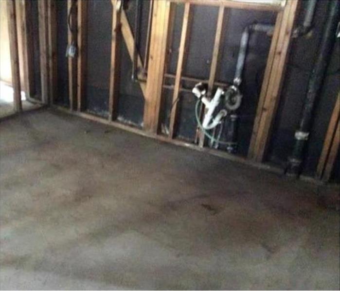 the kitchen area showing the plumbing in the wall of a framed only kitchen, no flooring, just the concrete surface