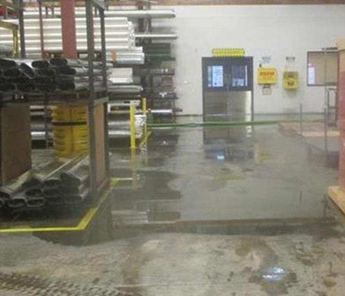 interior high-ceilinged warehouse with stacked pipes and hardware on shelving, water pooling on concrete floor