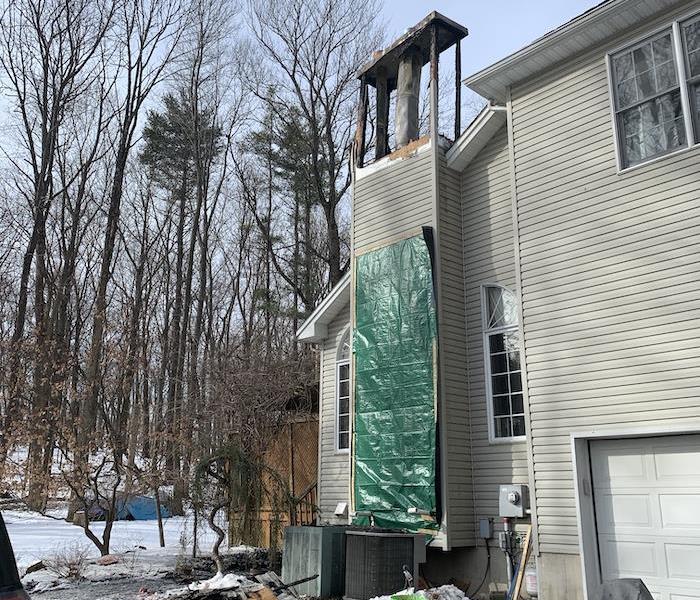 Chimney with tarp on home with debris in front of it