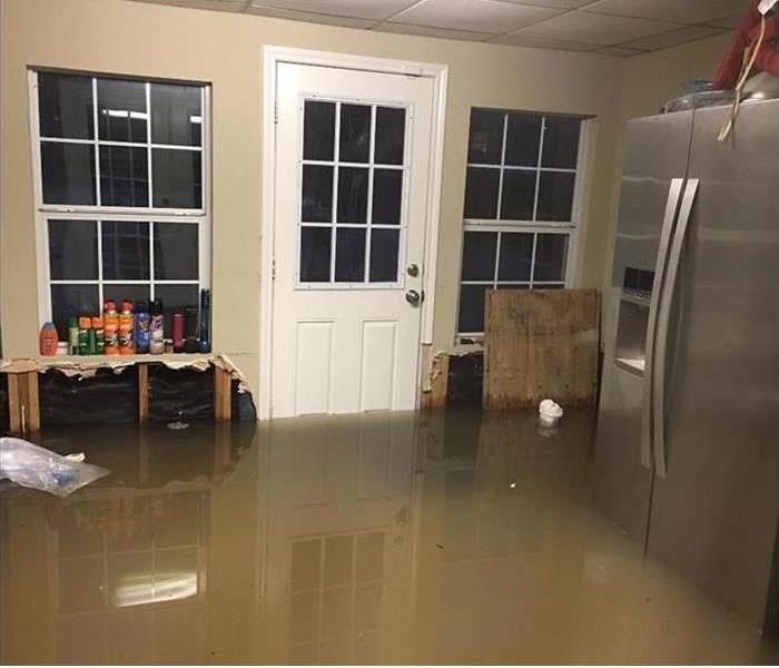 brown, dirty water covering sever inches, including a stainless steel fridge, in this room